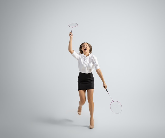 Une femme caucasienne en tenue de bureau joue au badminton sur fond gris