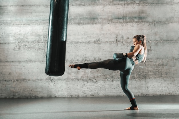 Femme caucasienne en tenue de sport et avec des gants de boxe sac de coups de pied dans la salle de gym.