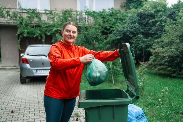 Photo femme caucasienne triant les ordures jetant un sac en papier usagé dans un petit bac à déchets à l'extérieur près d'un