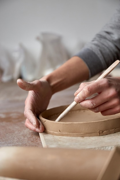 Femme céramiste travaillant dans un studio de poterie. Mains De Céramiste Sale D'argile. Processus de création de poterie. Maître céramiste travaille dans son atelier