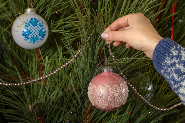 Femme en chandail décorant le sapin de Noël avec des boules de jouet