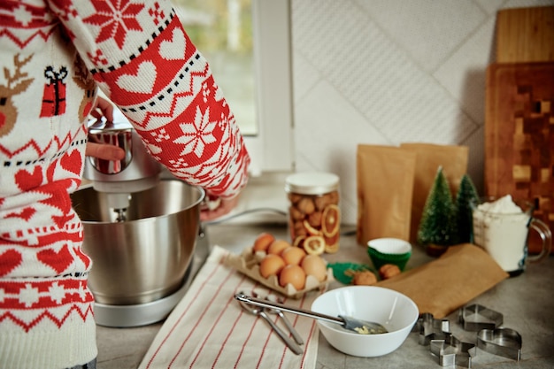 Femme en chandail de noël festif préparant la pâte pour les biscuits à la cuisine à la maison les mains des femmes utilisent elec