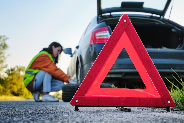 La femme change la roue endommagée de la voiture