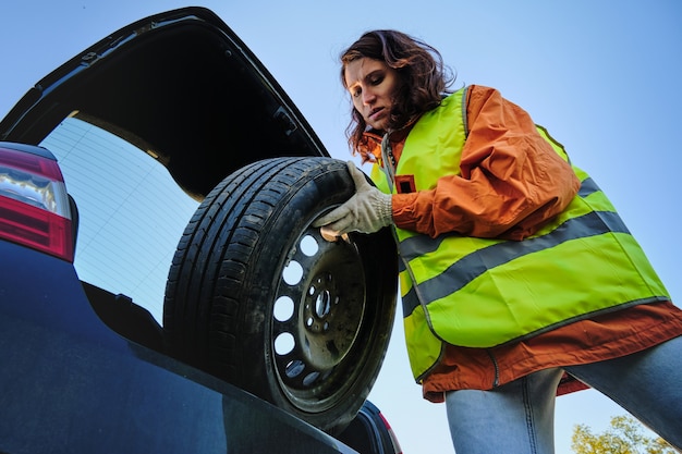 Photo la femme change la roue endommagée de la voiture