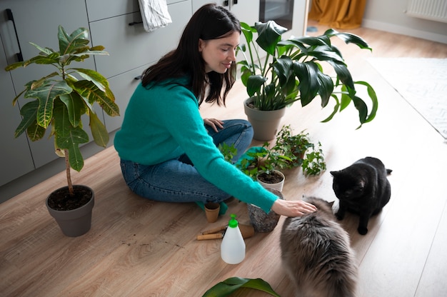 Femme changeant les pots de ses plantes et caressant ses chats à la maison pendant la quarantaine