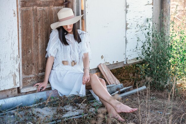 Photo une femme avec un chapeau assise contre le mur.