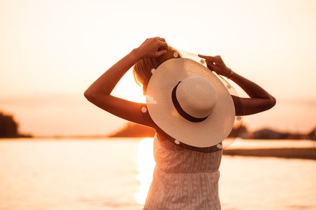 Une femme avec un chapeau au coucher du soleil de profil une jeune blonde en robe blanche et un chapeau de paille orné de...