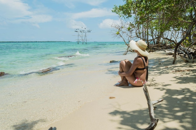 Femme avec chapeau et bikini assis en tailleur devant la plage de l'île de Cartagena Colombie