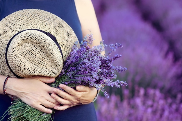 femme avec chapeau de paille et bouquet de lavande dans ses mains dans le champ de lavande en été.