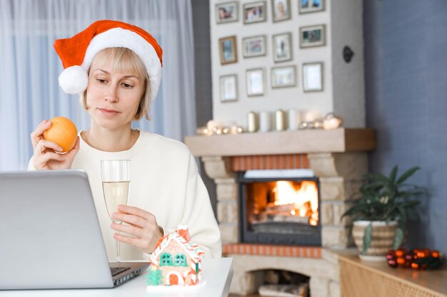 Une femme avec un chapeau de Père Noël tient une coupe de champagne parents et amis sur un ordinateur portable avec Noël
