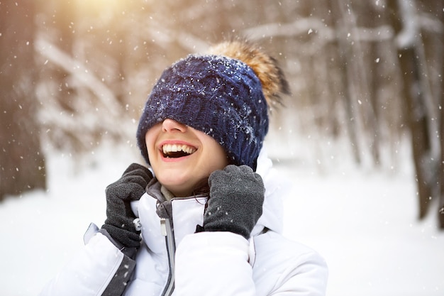 Femme avec un chapeau tricoté chaud tiré sur ses yeux sourit et aime la neige