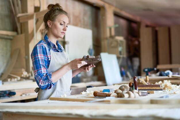 Femme charpentier tenant une pièce en bois en atelier