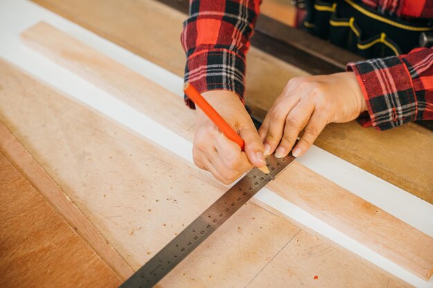 femme charpentière senior prenant la mesure d'une planche de bois et fabriquant dans l'atelier