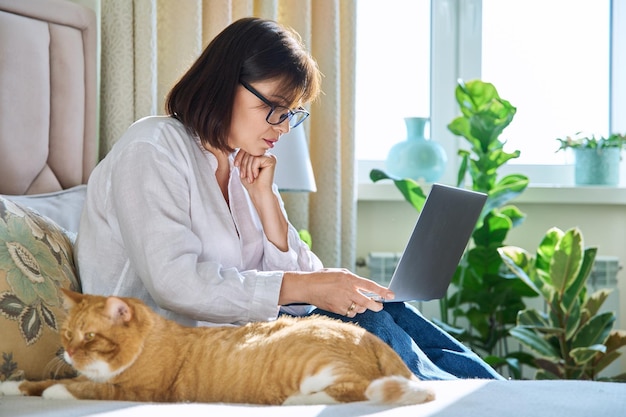 Femme avec chat assis sur le lit à la maison femme utilisant un ordinateur portable