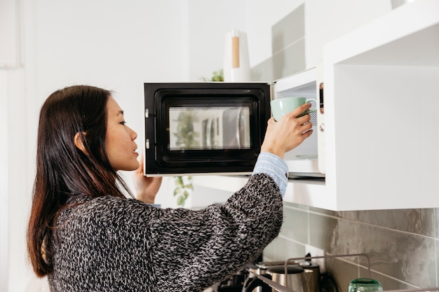 Femme chauffant la tasse avec boisson au micro-ondes