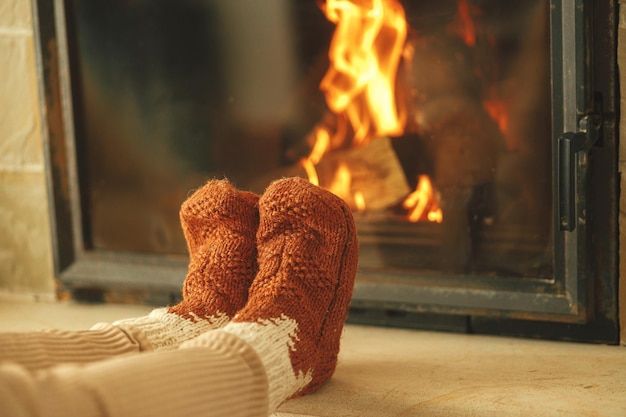Femme en chaussettes de laine confortables se réchauffant les pieds au foyer Chauffage maison avec poêle à bois