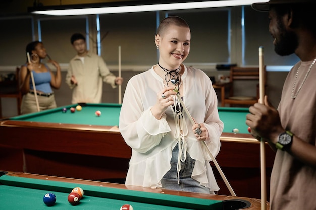 Une femme chauve jouant au billard avec des amis.