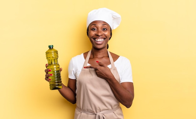 Femme chef afro noire à l'air excitée et surprise pointant vers le côté et vers le haut pour copier l'espace. notion d'huile d'olive