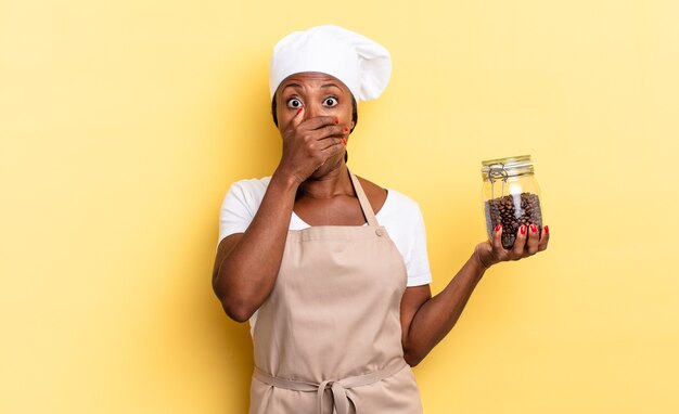 femme chef afro noire couvrant la bouche avec les mains avec une expression choquée et surprise, gardant un secret ou disant oups. concept de grains de café