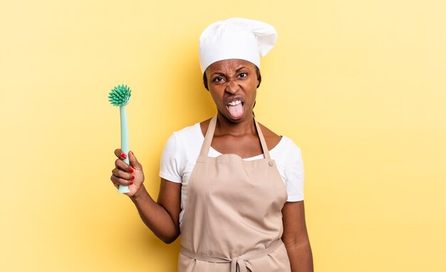 Femme chef afro noire se sentant dégoûtée et irritée, tirant la langue, n'aimant pas quelque chose de méchant et dégoûtant. concept de nettoyage de la vaisselle