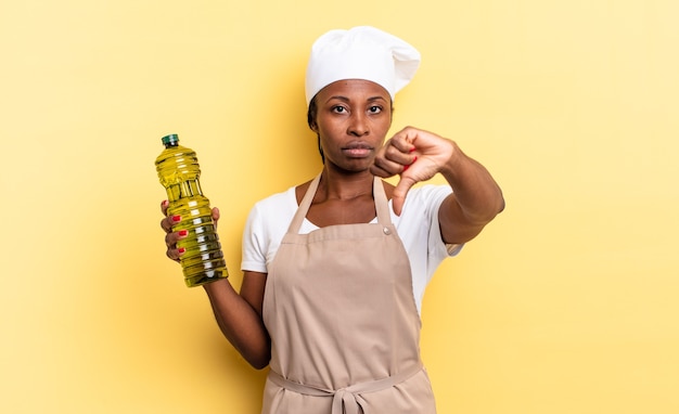 Femme chef afro noire se sentant fâchée, en colère, agacée, déçue ou mécontente, montrant les pouces vers le bas avec un regard sérieux. concept d'huile d'olive