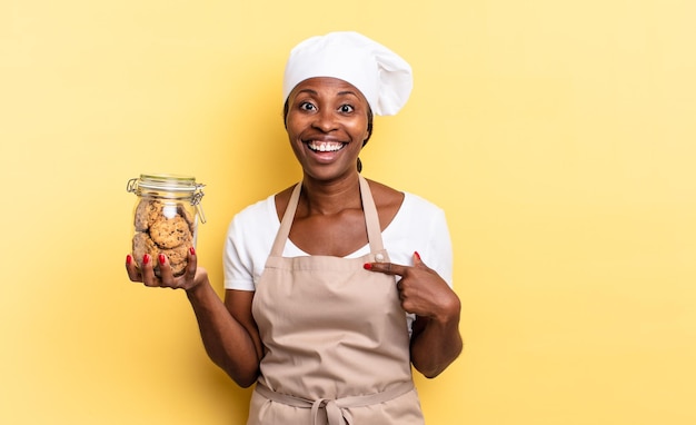 Femme chef afro noire se sentant heureuse, surprise et fière, se montrant elle-même avec un regard excité et étonné. notion de cookies