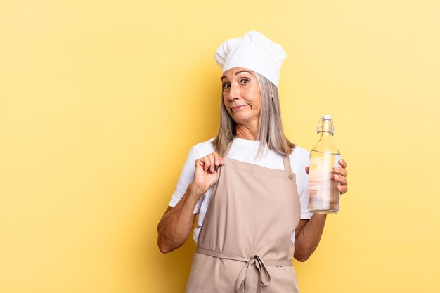 Femme chef d'âge moyen à l'air arrogante, réussie, positive et fière, pointant vers soi avec une bouteille d'eau