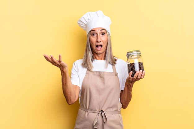 Femme chef d'âge moyen se sentant extrêmement choquée et surprise, anxieuse et paniquée, avec un regard stressé et horrifié tenant des grains de café