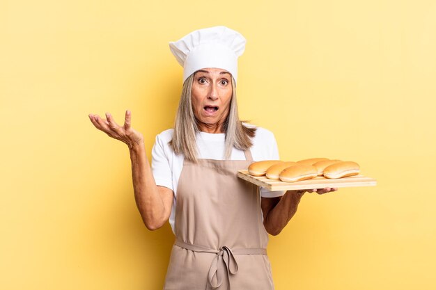 Femme chef d'âge moyen se sentant extrêmement choquée et surprise, anxieuse et paniquée, avec un regard stressé et horrifié et tenant un plateau à pain