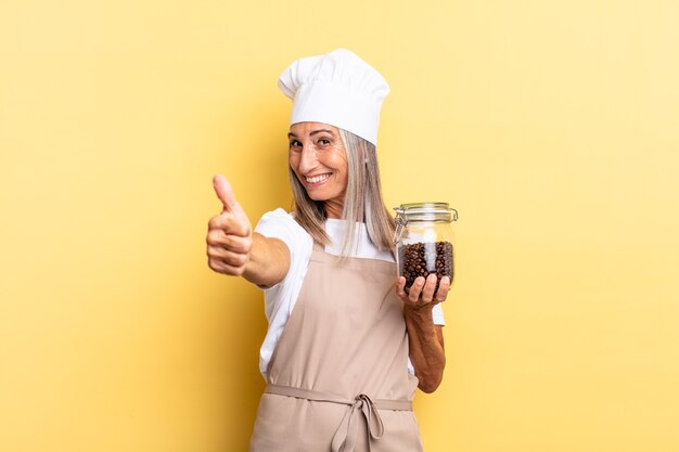 femme chef d'âge moyen se sentant fière, insouciante, confiante et heureuse, souriant positivement avec le pouce levé tenant des grains de café