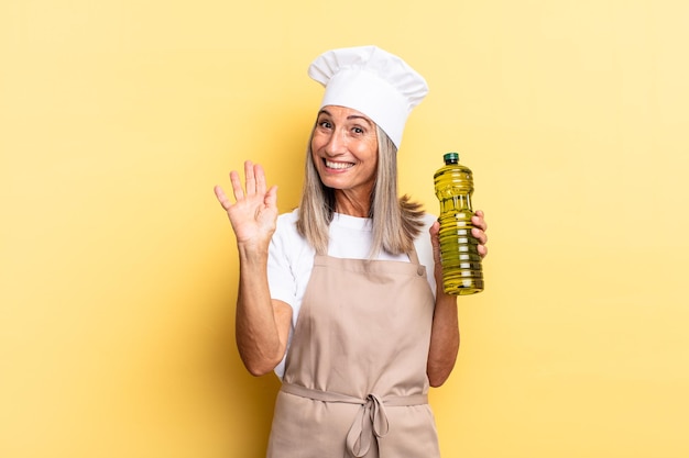 Femme chef d'âge moyen souriant joyeusement et joyeusement, agitant la main, vous accueillant et vous saluant, ou vous disant au revoir