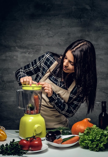 Femme chef brune préparant du jus de légumes dans un mélangeur.