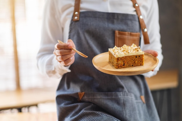 Une femme chef cuisinant et mangeant un morceau de gâteau aux carottes fait maison dans un plateau en bois