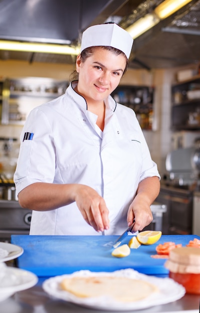 Femme chef prépare des crêpes au saumon et au caviar dans la cuisine du restaurant