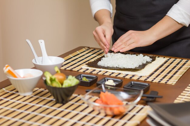 Femme chef remplissant des rouleaux de sushi japonais avec du riz