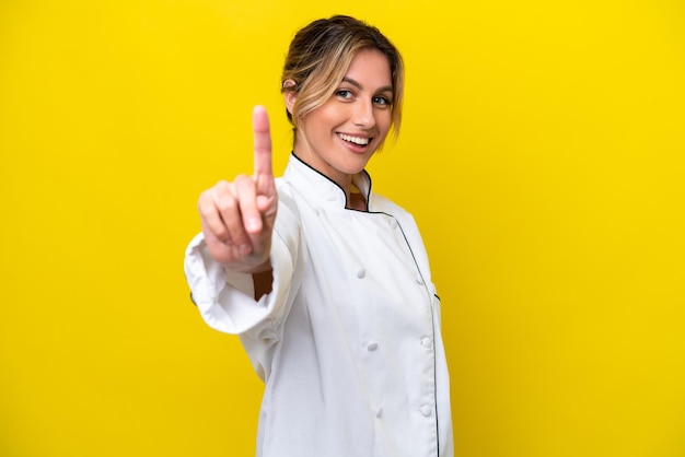 Femme chef uruguayenne isolée sur fond jaune montrant et levant un doigt