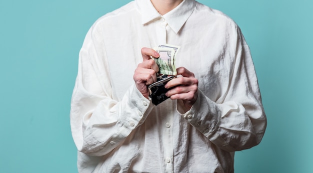 Femme en chemise blanche avec de l'argent et portefeuille sur mur bleu