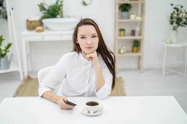 Une femme en chemise blanche boit du café dans un café Une employée de bureau pendant une pause déjeuner résout un problème commercial par téléphone Gestionnaire de niveau intermédiaire