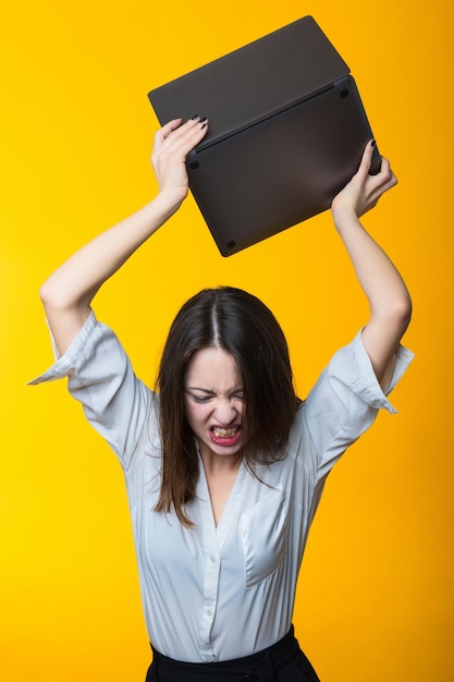 Une femme en chemise blanche veut casser un ordinateur portable Un portrait émotionnel en studio