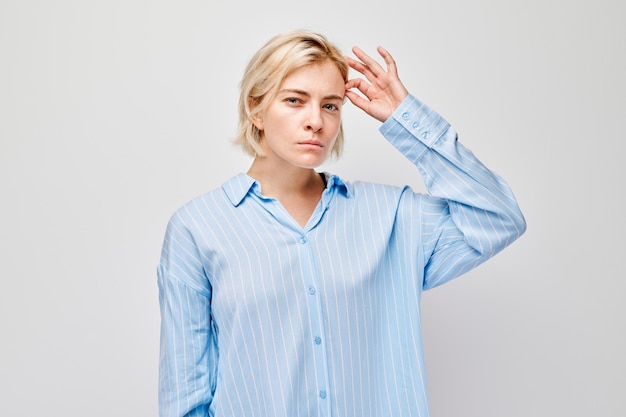 Femme en chemise bleue avec la main sur le front qui semble confuse oubliée isolée sur un fond clair