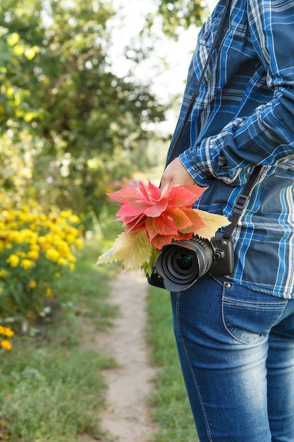 Femme en chemise à carreaux avec appareil photo tenant un bouquet de feuilles rouges sur fond de route rurale