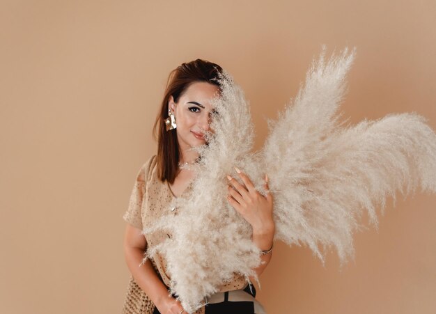 une femme en chemise pose sur un fond beige avec de grandes feuilles de roseau moelleuses