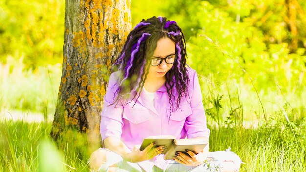 Une femme en chemise violette et lunettes lit une littérature sous un arbre une fille se repose avec un livre