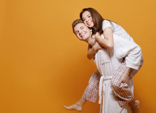 Femme chevauchant un petit ami, couple marié dans des vêtements à la maison sur fond jaune, relation heureuse, jeune femme embrasse l'homme