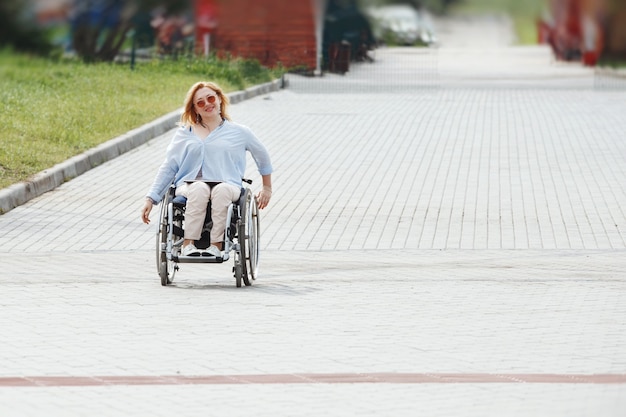 Femme chevauche un fauteuil roulant sur la route dans le parc d'été de la ville. Le concept d'un environnement accessible pour les personnes handicapées.