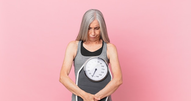 Femme de cheveux blancs d'âge moyen tenant une échelle de poids. concept de remise en forme et de régime