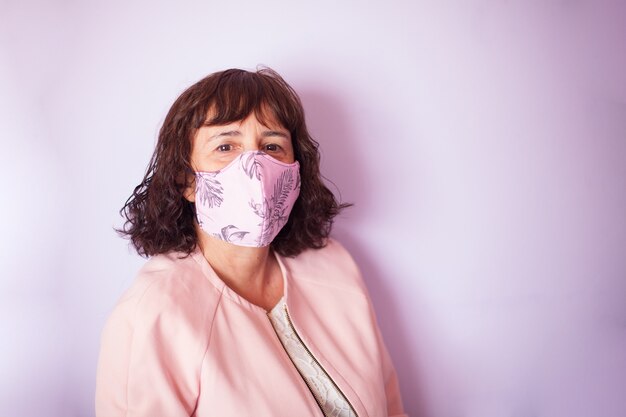 Femme cheveux bouclés d'âge moyen portant un masque rose sur fond rose