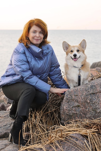 Femme cheveux roux avec un chien gallois corgi est assis sur les rochers