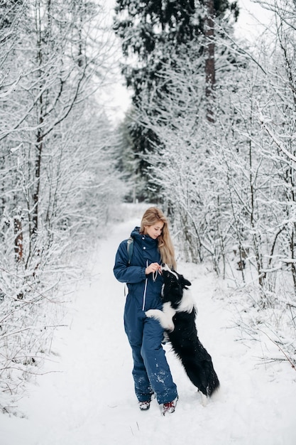 Femme avec un chien border collie dans la forêt enneigée