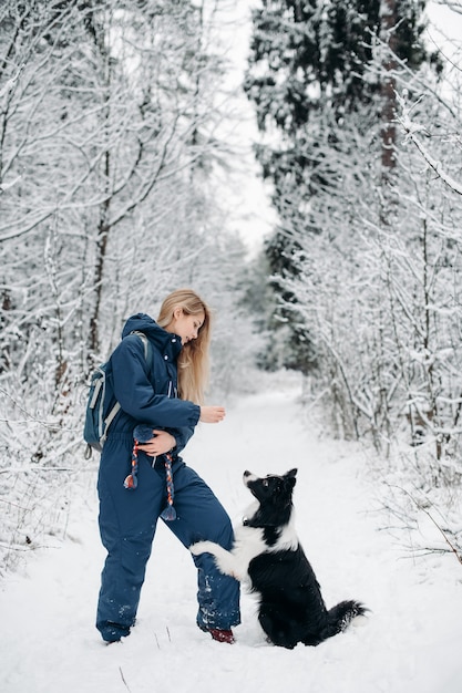 Femme avec un chien border collie noir et blanc dans la forêt enneigée